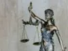 Die Justizia-Figur, Symbol für Gerechtigkeit und Recht. Ihre Augenbinde steht für Unparteilichkeit, die Waage für ausgewogene Urteile. In ihren Händen trägt sie das Schwert der Strafe und das Gesetzbuch der Rechtsprechung – ein kraftvolles Symbol für Fairness und Rechtsstaatlichkeit.
